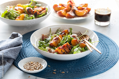 Grilled peach and arugula salad with more peaches in behind against a bright sunny window.