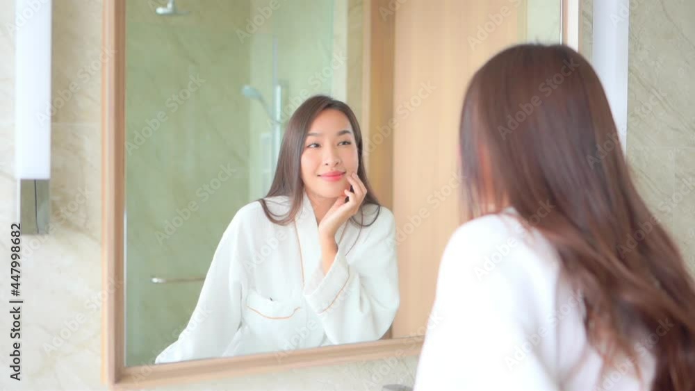 Asian woman in hotel bathrobe checking and touching her pretty face near the mirror in the bathroom slow-motion Asian woman in hotel bathrobe checking and touching her pretty face near the mirror in the bathroom slow-motion