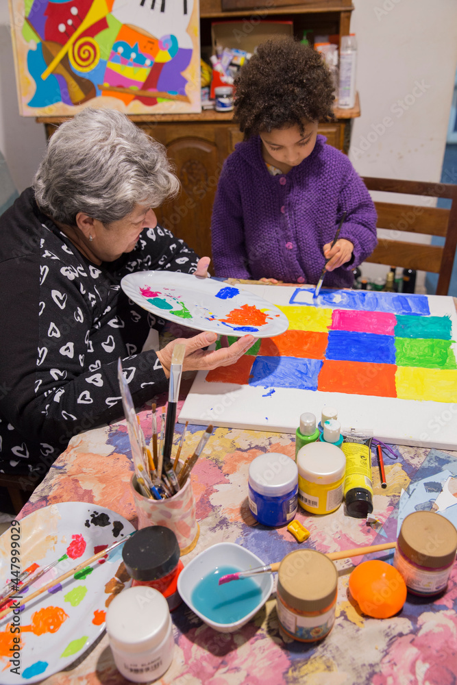 Grandma teaching painting to granddaughter . Grandma teaching painting to granddaughter .