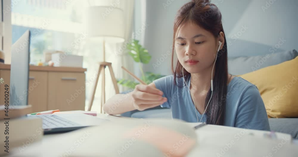 Young Asia girl teenager with casual wear headphones use laptop computer learn online write lecture notebook in living room at house. Isolate education online e-learning coronavirus pandemic concept. Young Asia girl teenager with casual wear headphones use laptop computer learn online write lecture notebook in living room at house. Isolate education online e-learning coronavirus pandemic concept.