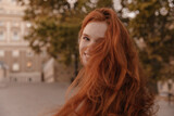 Close-up portrait of young girl smiling and waving hair outdoors. Pretty fluffy ginger at city in autumn
