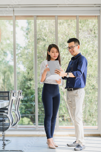 Happy Asian businessman and woman discussing new business project in tablet in modern meeting room.