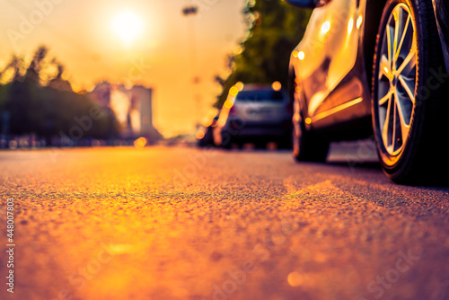 Sunset in the city, the empty road with parked cars. Close up view from the level of a parked car wheels