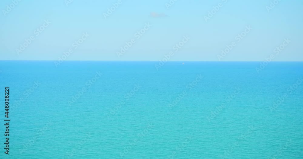 Distant View Of A Lone Boat Sailing Across The Bright Blue Sea In Summer. wide aerial Distant View Of A Lone Boat Sailing Across The Bright Blue Sea In Summer. wide aerial