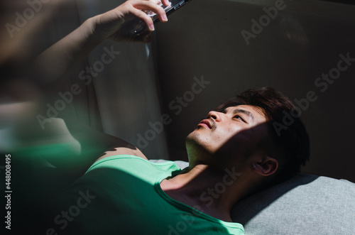 Portrait of pensive young handsome Chinese man lying on floor and looking away