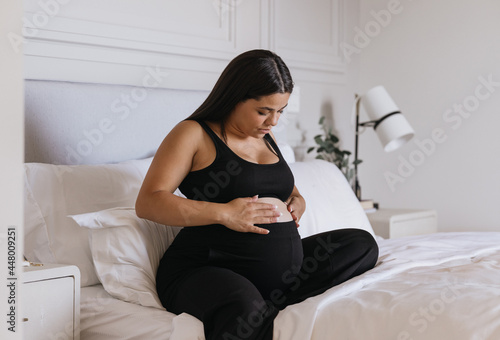 Pregnant Carribbean Indigenous woman practicing self care and putting lotion on baby bump in bed