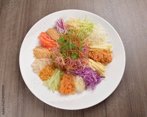 Chinese New Year festival colourful Yu Sheng Lo Hei salad with smoked salmon fish, cracker cookies and sweet sauce on wood background asian halal menu photo