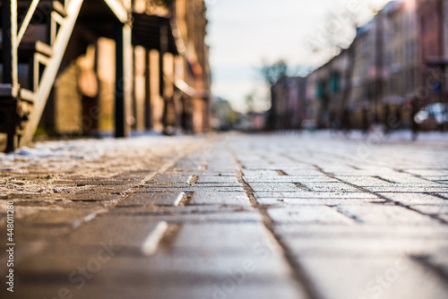 Bright winter sun in a big city, empty street with snow. Close up view from the sidewalk level