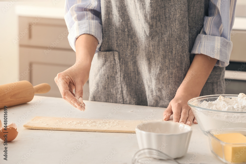 Woman sprinkling dough with flour on kitchen table Woman sprinkling dough with flour on kitchen table