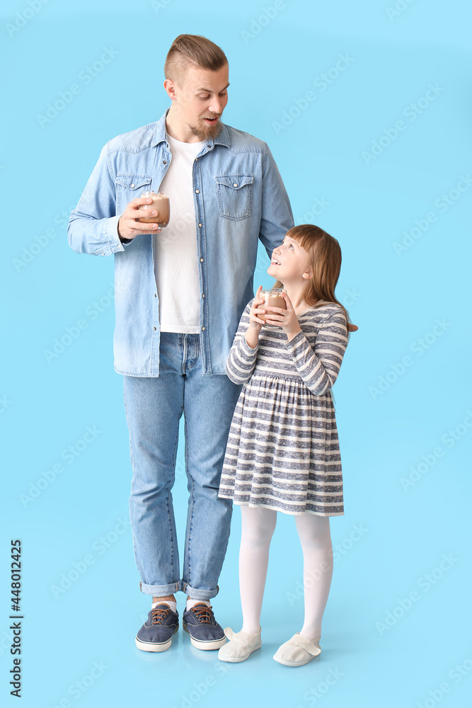 Happy daughter and father with cups of hot cocoa on color background