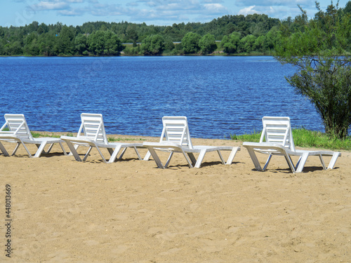 White sun loungers on the sandy shore of the reservoir summer vacation.