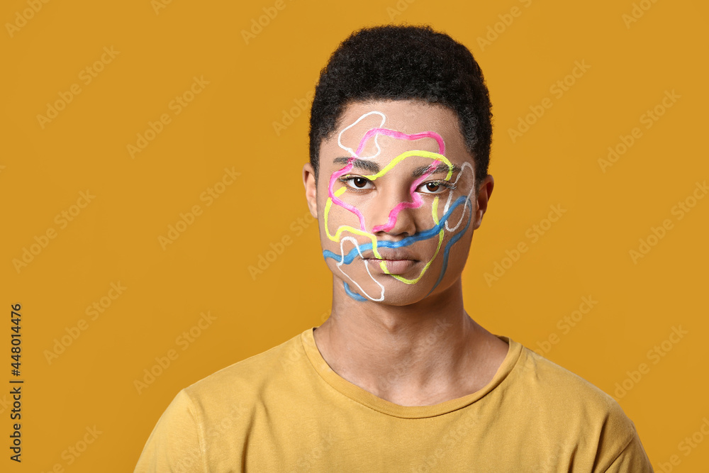 Young African-American guy with paint on face against color background