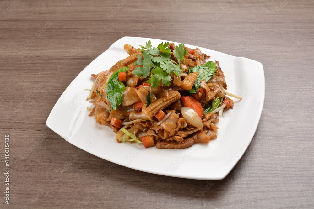 wok stir fried kway teow rice noodle mee goreng with vegetable in spicy soy chilli sauce on wood background asian halal vegan menu