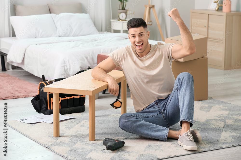 Happy young man assembling furniture at home Happy young man assembling furniture at home