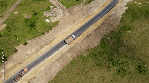 Heavy mining dump truck unloads sand for construction new paved road and bulldozer goes in reverse. Concept of development new territories and laying highways