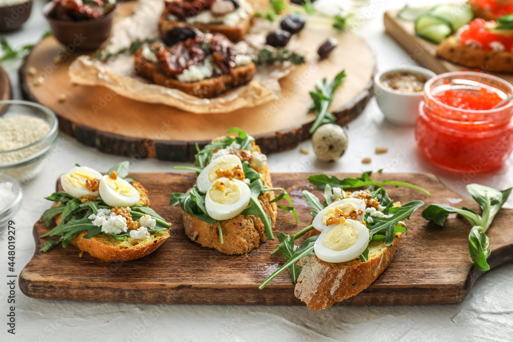 Tasty bruschettas with cheese, eggs and arugula on light background