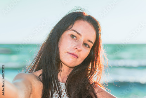 Happy brunette woman making selfie on beach.Summer holiday evening,closeup,blured sea or ocean background. © ARVD73