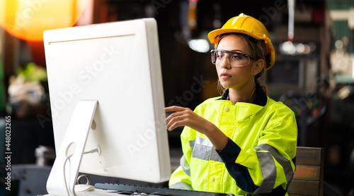 Female Quality control inspector checking workers at factory. Woman engineer with yellow hard hat helmet working on desktop computer inside factory