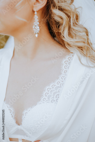 The bride puts on beautiful wedding earrings. Girl with hairstyle with curls wears jewelry accessories