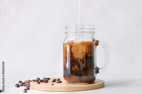 Pouring of milk into mason jar with hot coffee and beans on white background