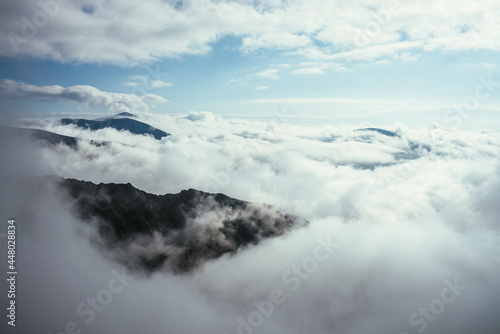 Wonderful alpine scenery with great rocks and mountains in dense low clouds. Atmospheric highlands landscape with mountain tops above clouds. Beautiful view to snow mountain peaks over thick clouds.