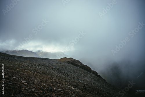 Dark atmospheric landscape on edge of abyss in highlands. Dangerous mountains and abyss among low clouds. Danger mountain pass and sharp rocks in clouds. Dangerous cloudy rainy weather in mountains.