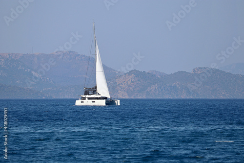 One-masted sailing yacht in the sea. White sailboat on misty mountains background