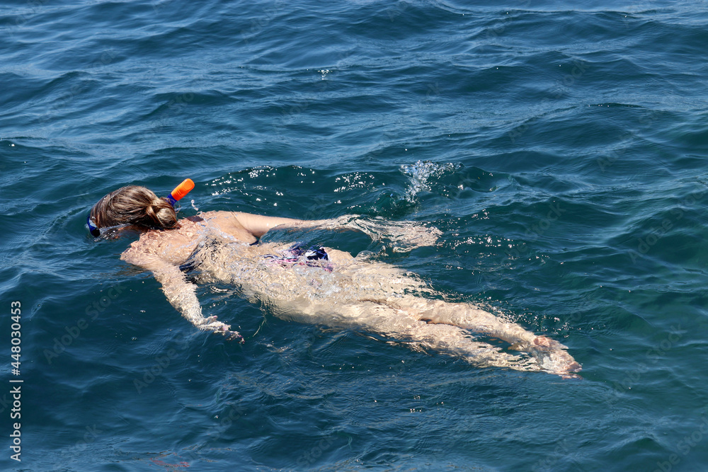 Snorkeling in the sea, girl in bikini and diving mask swims in emerald water