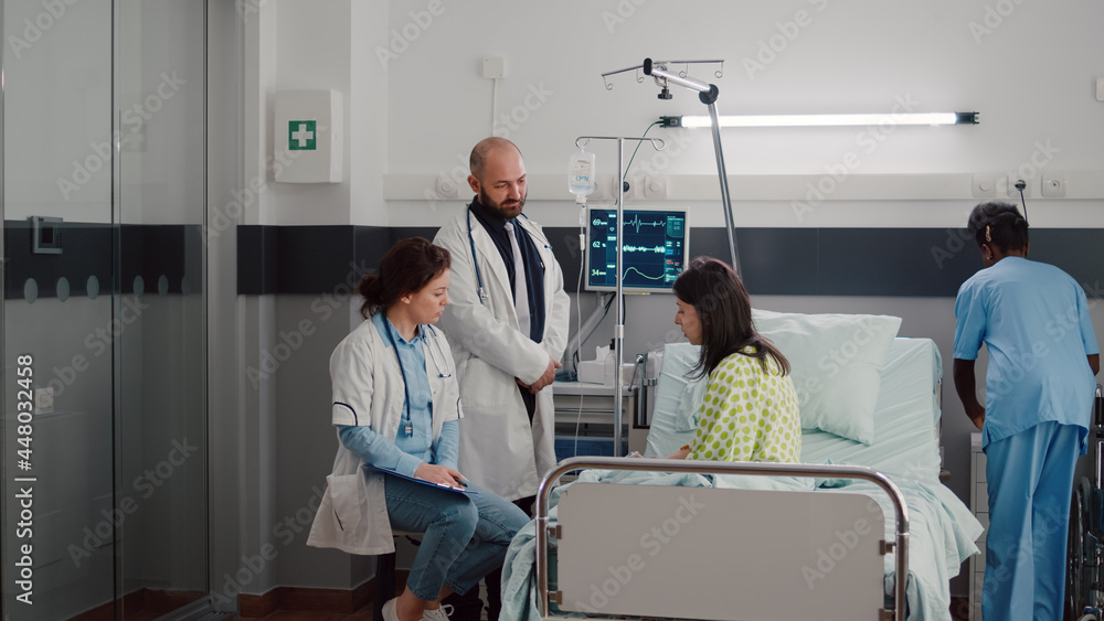 Obraz premium Specialist practitioner doctors monitoring sick man explaining illness treatment while working in hospital ward. Patient sitting in bed discussing symptom disease during recovery appointment