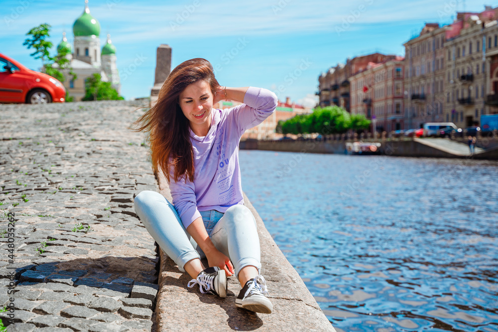 A young woman walks along the embankment in St. Petersburg with beautiful views of bridges and canals.