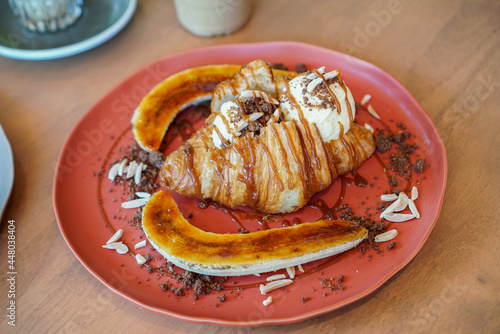 Banana caramel croissant. A plain croissant topped with vanilla ice cream scoop, serving with banana caramelized , almond sliced and chocolate crumble.