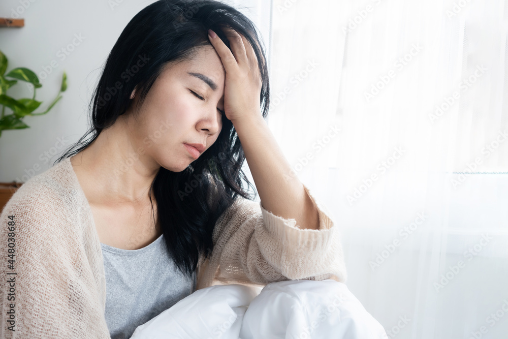 Asian woman having headache migraine, hangover, lack of sleep sitting in bed after wake up in the morning Asian woman having headache migraine, hangover, lack of sleep sitting in bed after wake up in the morning