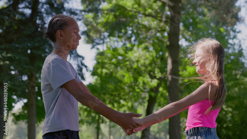 Side view of caucasiangirl and african boy hold hands standing together in park photo
