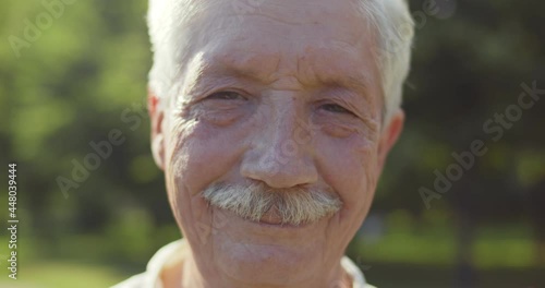 Bokeh close up portrait of happy senior man looking at camera outdoors photo