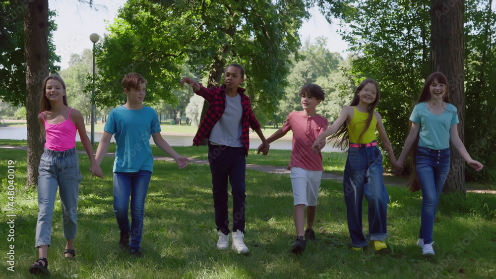 Obraz premium Multiethnic preteen kids hold hands and walk in park together