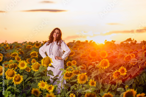Beautiful woman enjoying nature in the sunflower field at sunset. Traditional clothes. Attractive brunette woman with long and healthy hair.