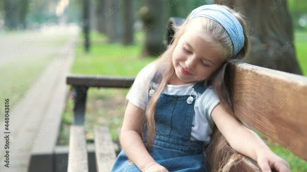 Small tired child girl sitting on a bench with closed eyes resting in summer park. Small tired child girl sitting on a bench with closed eyes resting in summer park.