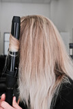 A woman does her hair with a curling iron and gives straight hair a wavy texture and volume.