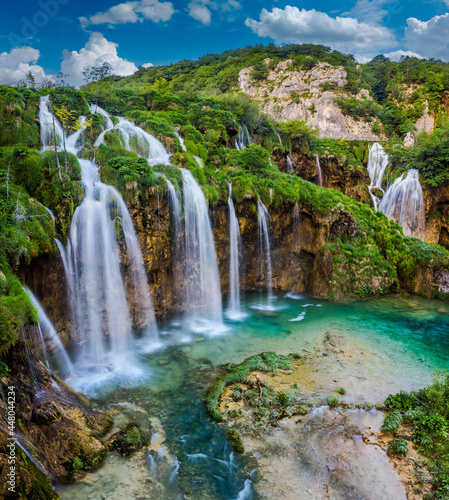Plitvice  Croatia - Beautiful waterfalls of Plitvice Lakes  Plitvi  ka jezera  in Plitvice National Park on a bright summer day with blue sky and clouds and green foliage and turquise water
