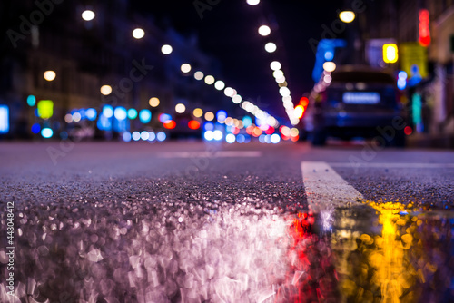 Nights lights of the big city, the main city street with parked car. Close up view from the level of the dividing line