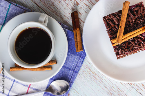 Cake with cinnamon and a cup of coffee on a wooden table in a close-up top view