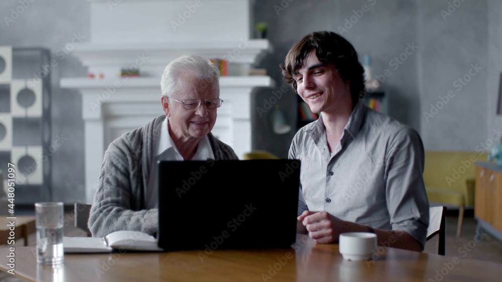 Grandson teach grandfather to work with computer sitting together in living room Grandson teach grandfather to work with computer sitting together in living room