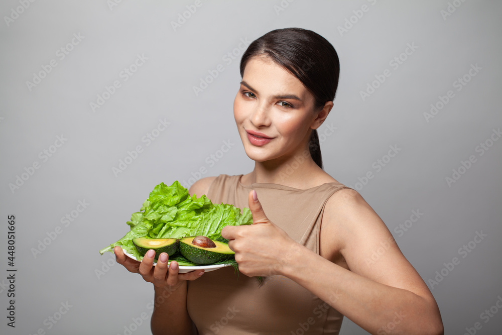 Happy woman showing thumb up and holding green avocado with salad. Detoxification, vegetarian, healthy eating and diet concept Happy woman showing thumb up and holding green avocado with salad. Detoxification, vegetarian, healthy eating and diet concept