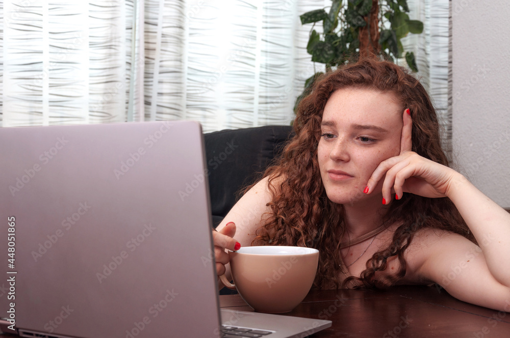 Fototapeta premium Portrait of young redhead with serious face looking at her computer screen.