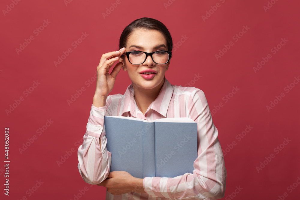 Surprised young woman brunette wearing glasses holding book with mockup copy space