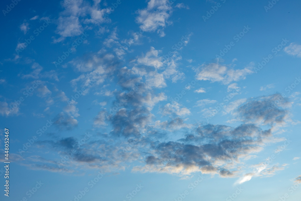 Obraz premium Sunset soft tones enlighten a flock of small cumulus clouds contrasting against a blue vibrant sky. Weather conditions and climate concept. Abstract background wallpaper poster.