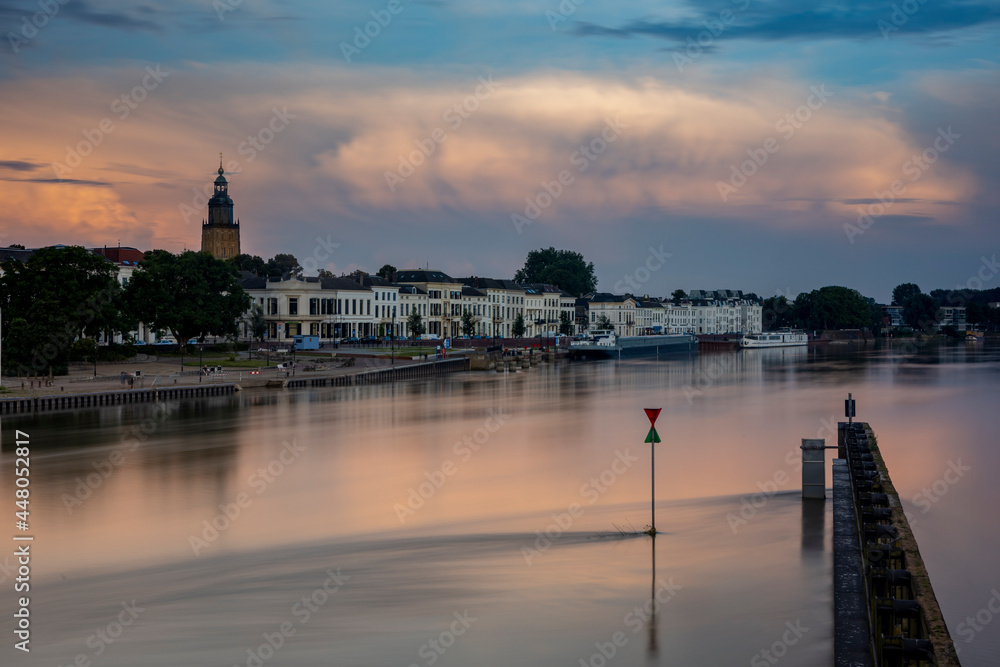 Long exposure cityscape of Zutphen in The Netherlands with large cumulonimbus rain cloud above in colorful sunset tones. Dutch climate and weather condition landscape.