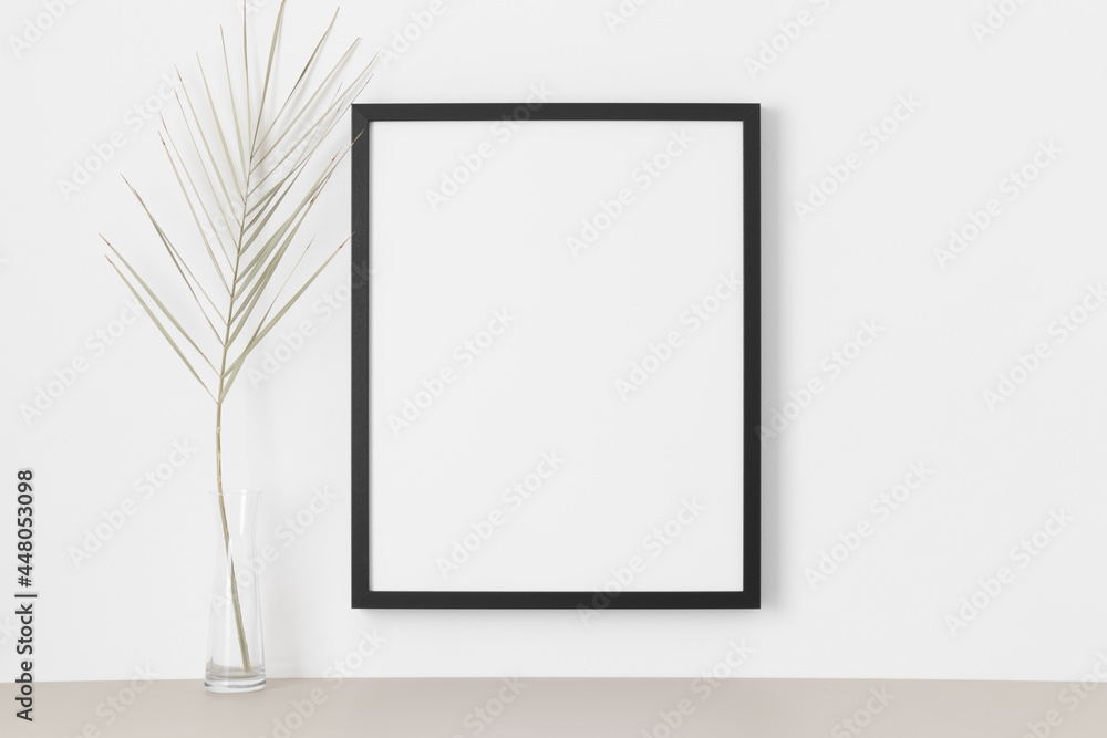 Black frame mockup on the wall with a palm leaf. Black frame mockup on the wall with a palm leaf.