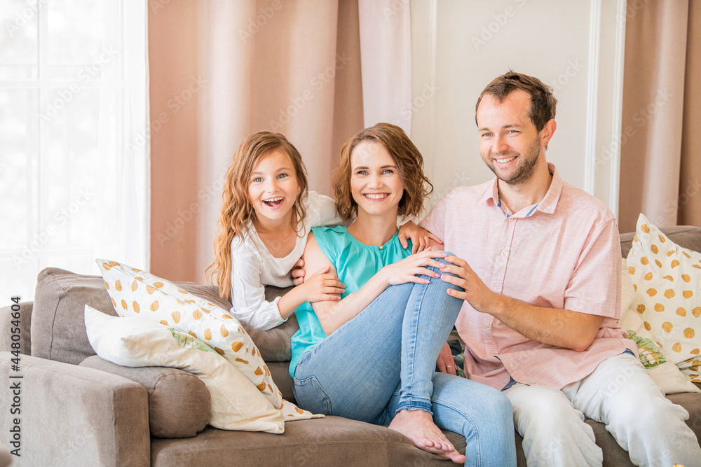 Happy family, mom dad and daughter are sitting on couch and laughing together