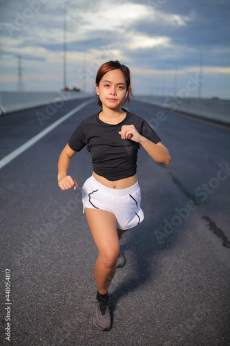 Young fitness Asian woman wear a black shirt and white shorts. is stretching in  and jogging an outdoor workout on the city road in the for lifestyle health.